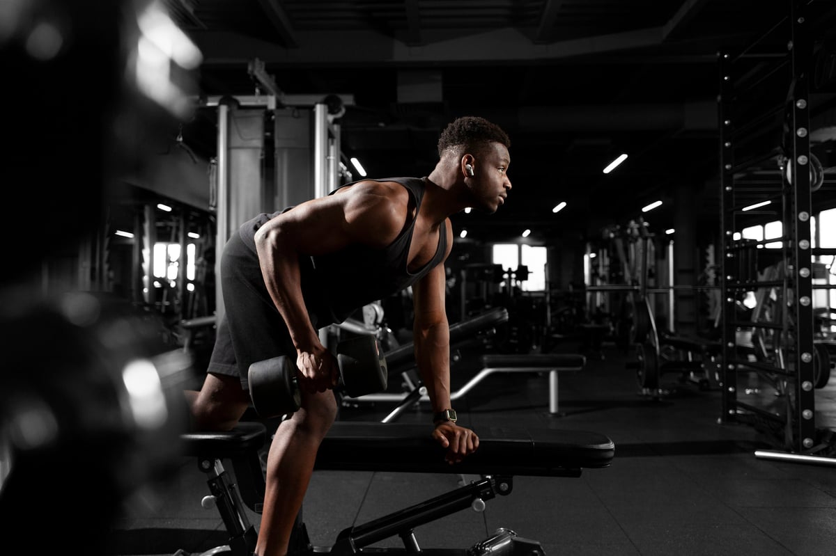 young athletic african american man trains in dark gym, athletic guy lifts heavy dumbbells in fitness club