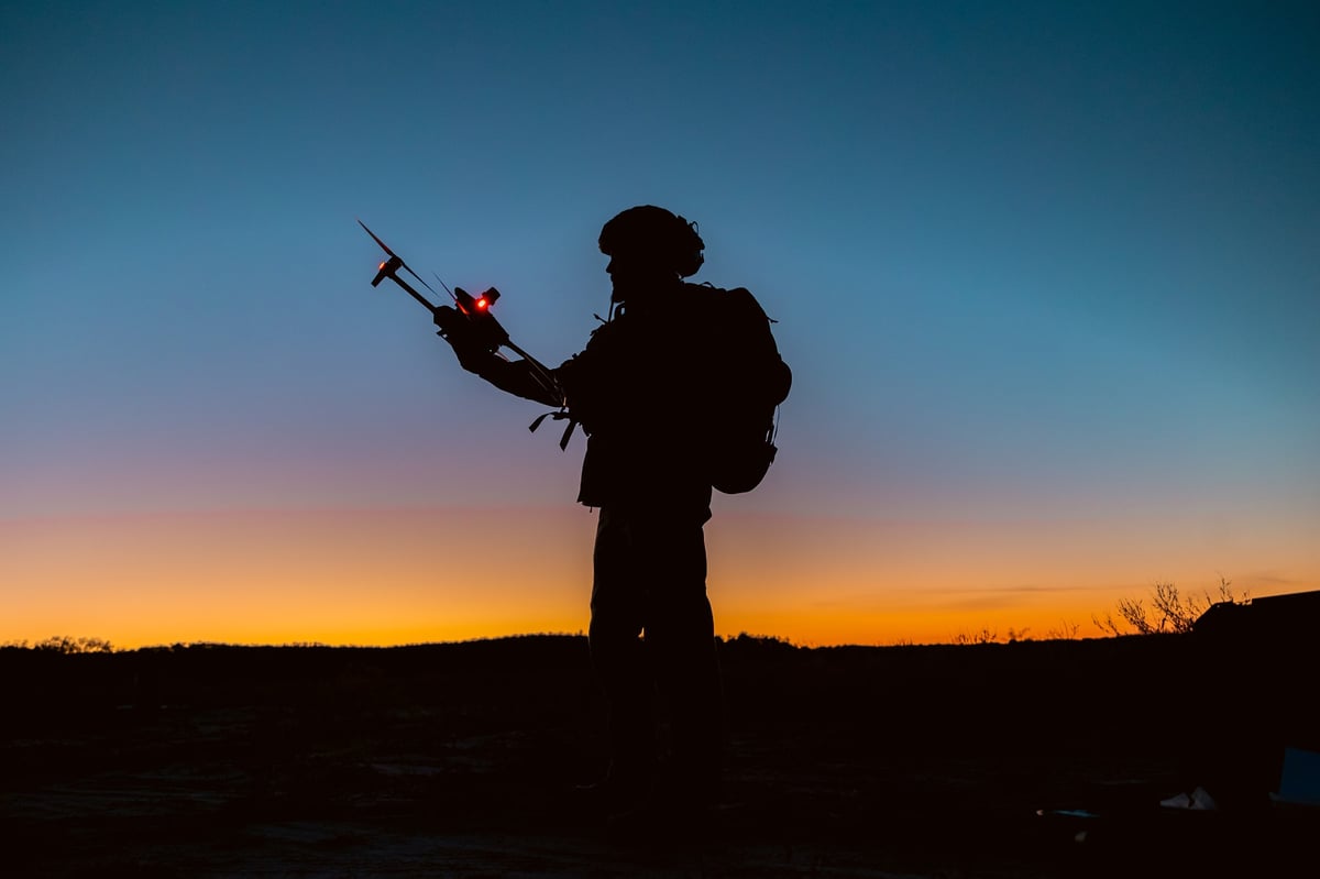 Silhouettes of soldiers are using drone for scouting during military operation against the backdrop of a sunset